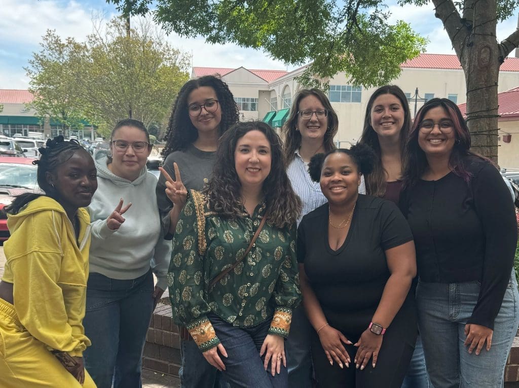 A group of smiling, diverse women posing outside of a shopping center