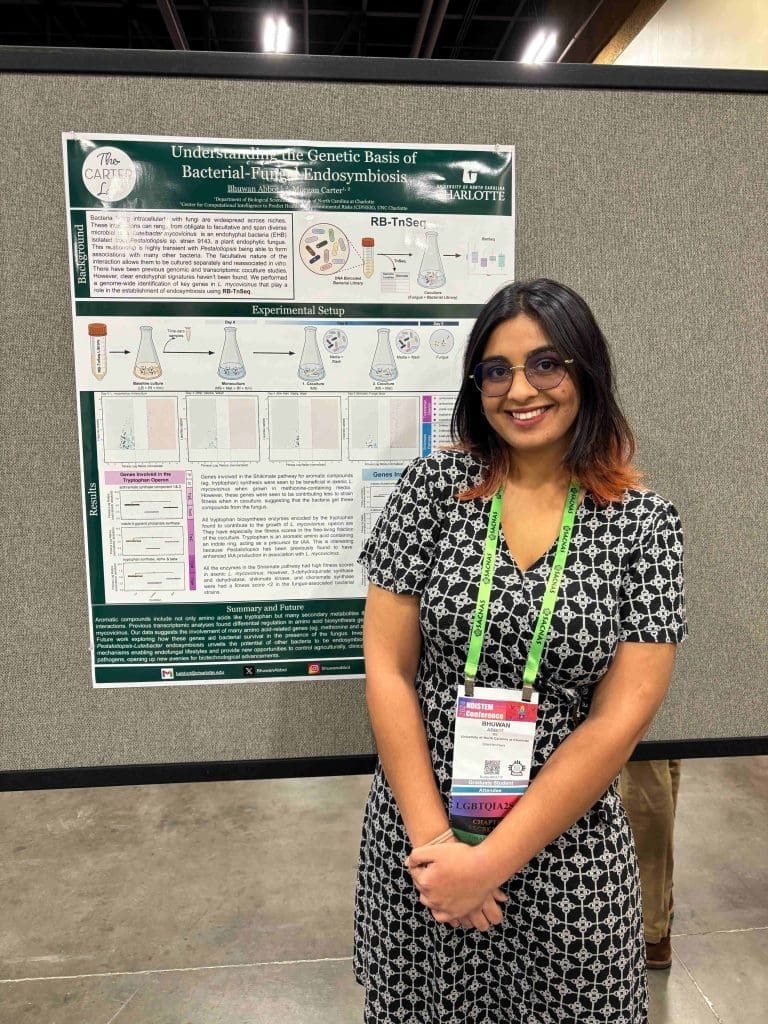 An Indian woman with a conference badge on smiling in front of a scientific poster