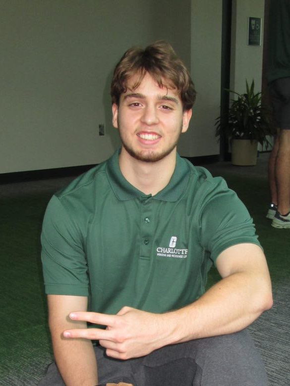 Photo of a young white man in a Charlotte green polo smiling