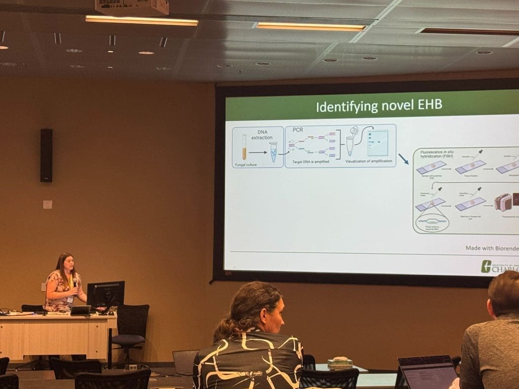 A woman giving a talk in front of a powerpoint slide that says "Identifying novel EHB"